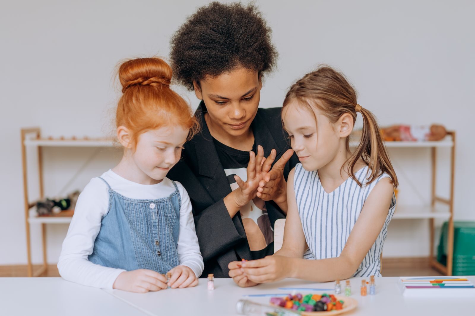 A teacher guiding children in creative activities in a diverse classroom setting.